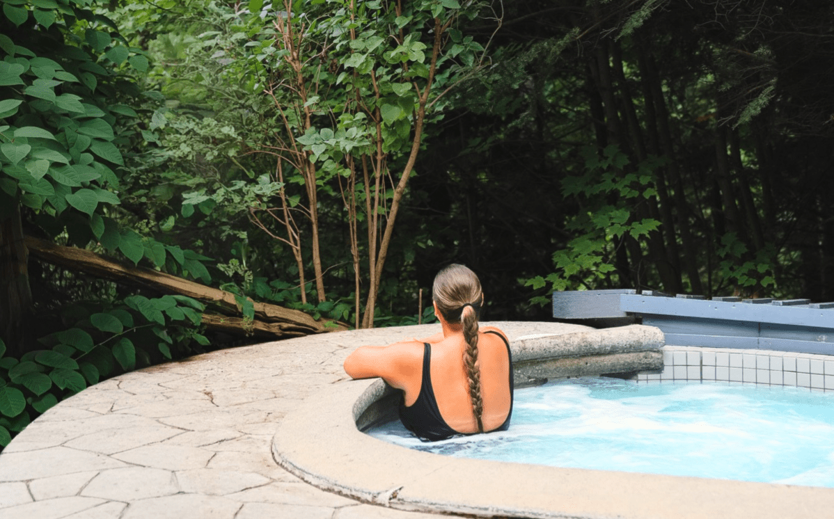 Personne en maillot relaxant dans un spa extérieur en pleine nature, entouré d’arbres et de verdure, ambiance détente et bien-être en forêt