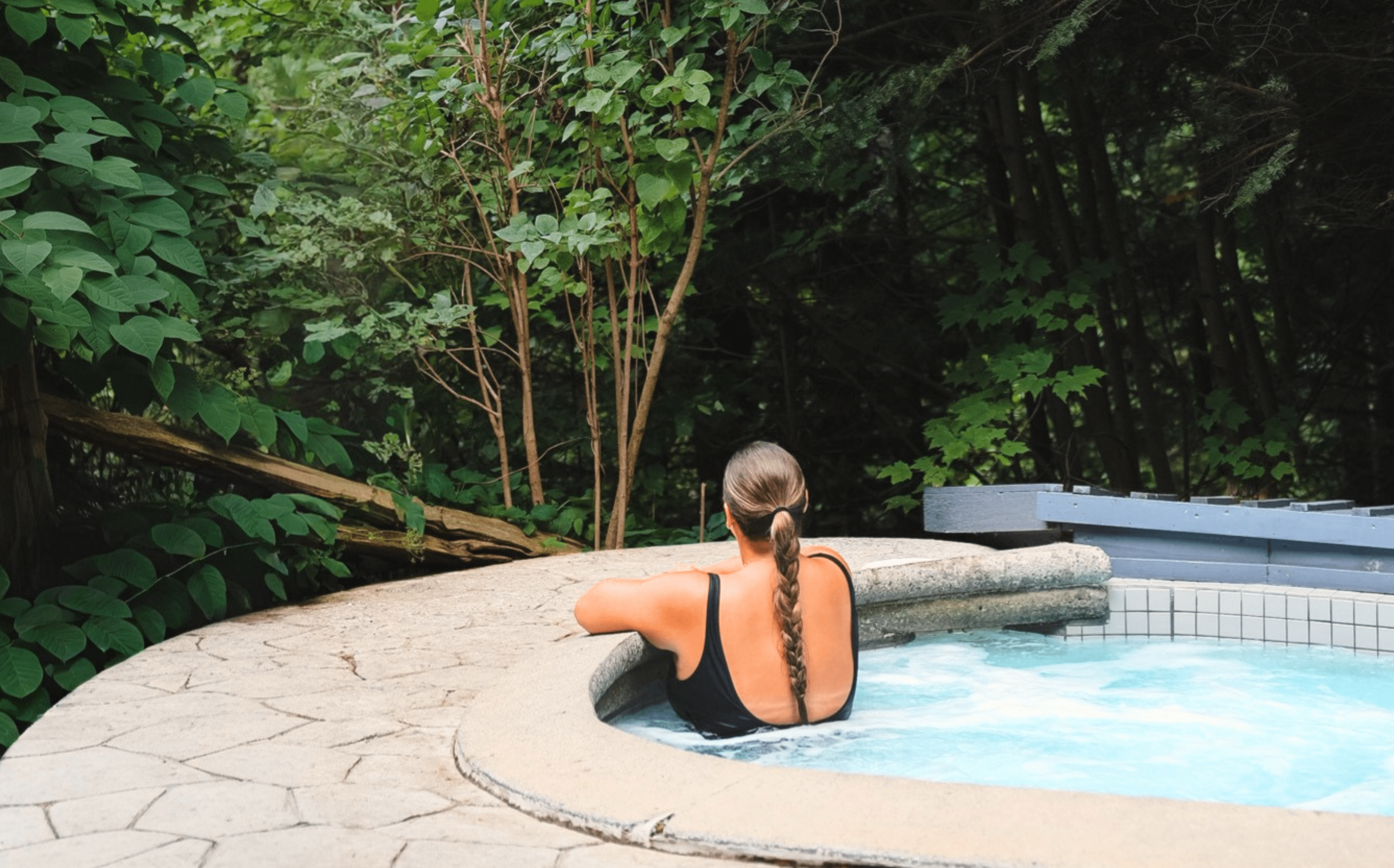 Personne en maillot relaxant dans un spa extérieur en pleine nature, entouré d’arbres et de verdure, ambiance détente et bien-être en forêt
